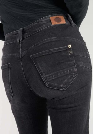 Jean en denim noir taille haute, avec une patch en cuir marron, des coutures complexes sur les poches arrière et une coupe slim.