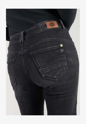Jean en denim noir taille haute, avec une patch en cuir marron, des coutures complexes sur les poches arrière et une coupe slim.