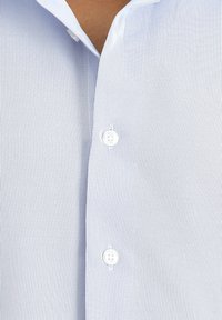 Koszula zapinana na guziki w pionowe jasnoniebieskie paski, z białymi guzikami i miękką bawełnianą fakturą. Cechuje się wyrazistym kołnierzykiem i minimalistycznym designem.