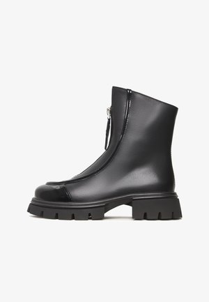 Botas ankle negras con puntera brillante, parte superior texturizada, cremalleras laterales y suelas de goma gruesa con un dibujo profundo para mayor agarre.