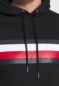 Sudadera negra con un diseño frontal de rayas horizontales en rojo, blanco y azul marino, con detalles plateados en los cordones.