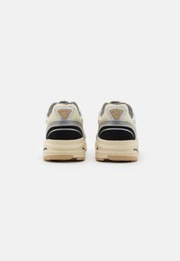 Semleges színű sneaker, hálós felsőrésszel, fekete velúrrészletekkel és bézs gumitalppal. A saroknál logóval és fekete csíkokkal rendelkezik.