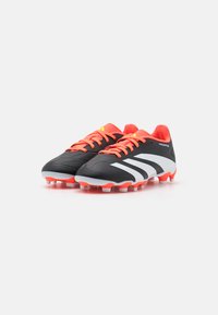 Botas de fútbol negras con cordones y acentos de color naranja brillante, presentando una parte superior texturizada, rayas blancas y una suela moldeada con tacos.