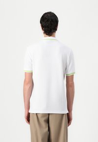 Polo shirt bianco a maniche corte con un accento verde sul colletto e sulle maniche, realizzato in un tessuto morbido, con una vestibilità rilassata e un design classico.
