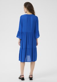 Abito blu a strati con maniche lunghe e svasate e vita arricciata. Tessuto leggero con una texture liscia e una sottile lucentezza.