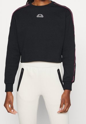 Felpa nera corta con logo circolare, strisce laterali rosa e polsini a coste, abbinata a pantaloni da jogging chiari con tasche con zip.