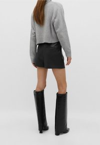 Suéter de punto corto gris, pantalones cortos de cuero sintético negro y botas negras con tacón hasta la rodilla. Texturas suaves, diseño ajustado, sin patrones visibles.