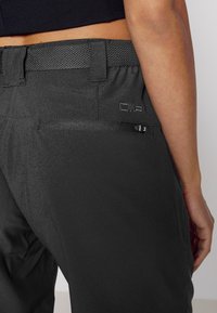 Musta housu, jossa on kuvioitu kangas, leveä joustava vyötärönauha, vetoketjullinen tasku ja CMP-logo painettuna lähelle vyötärönauhaa.