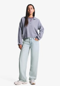 Svijetlo sivi pleteni pulover s ovratnikom, uparen s laganim plavim trapericama širokog kroja. Bijele tenisice s bež detaljima upotpunjuju odjevnu kombinaciju.