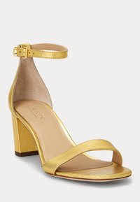 Zlaté metalické sandály na vysokém podpatku s otevřenou špičkou a silným blokovým podpatkem, nártní pásek s přezkou a hladká podšívka.