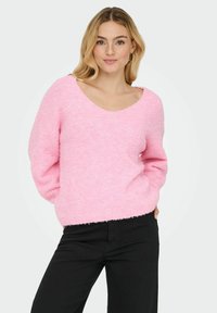 Roza puhasta pulover z okroglo obrobo in dolgimi rokavi, ki ima sproščen kroj in teksturirano tkanino. Obujte ga s črnimi hlačami.