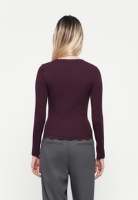 Top bordeaux à manches longues en tissu côtelé avec une finition en dentelle au niveau du col et de l'ourlet, associé à un pantalon gris sur mesure.