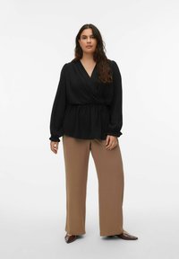 Czarna bluzka kopertowa z luźnymi rękawami i marszczonym pasem, zestawiona z szerokimi brązowymi spodniami i butami z zaostrzonymi noskami. Prosty, teksturowany wzór.