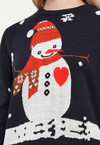 Knit sweater featuring a snowman design with a red scarf, hat, and heart, on a dark blue background with white snowflakes.