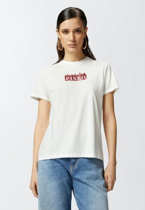 T-shirt bianca in cotone con maniche corte e scollatura a girocollo, con logo rosso "PINKO" stampato sul petto, abbinata a jeans in denim azzurro.