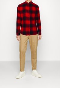 Rood en zwart geruite flanellen overhemd met knopen, gecombineerd met kaki broek en witte sneakers. Glad materiaal en een getailleerde pasvorm.