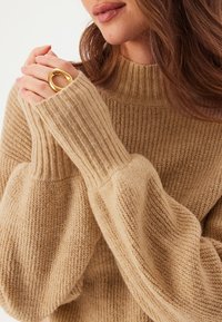 Beige gestrickter Pullover mit hohem Kragen, Rippdetails an den Bündchen und einer weichen Textur, der lockere, voluminöse Ärmel hat.
