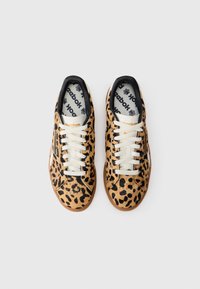 Tenisice s leopard uzorkom imaju gornji dio od teksturirane smeđe tkanine, crne akcente, bijele vezice i gumeni potplat s Reebok logom sa strane.