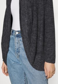 Cardigan grigio scuro, con texture, dalla vestibilità ampia, davanti aperto e morbido tessuto abbinate a jeans chiari a vita alta.