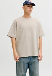T-shirt beige oversize en coton, avec des manches courtes et un col ras du cou, associé à un jean en denim bleu clair.