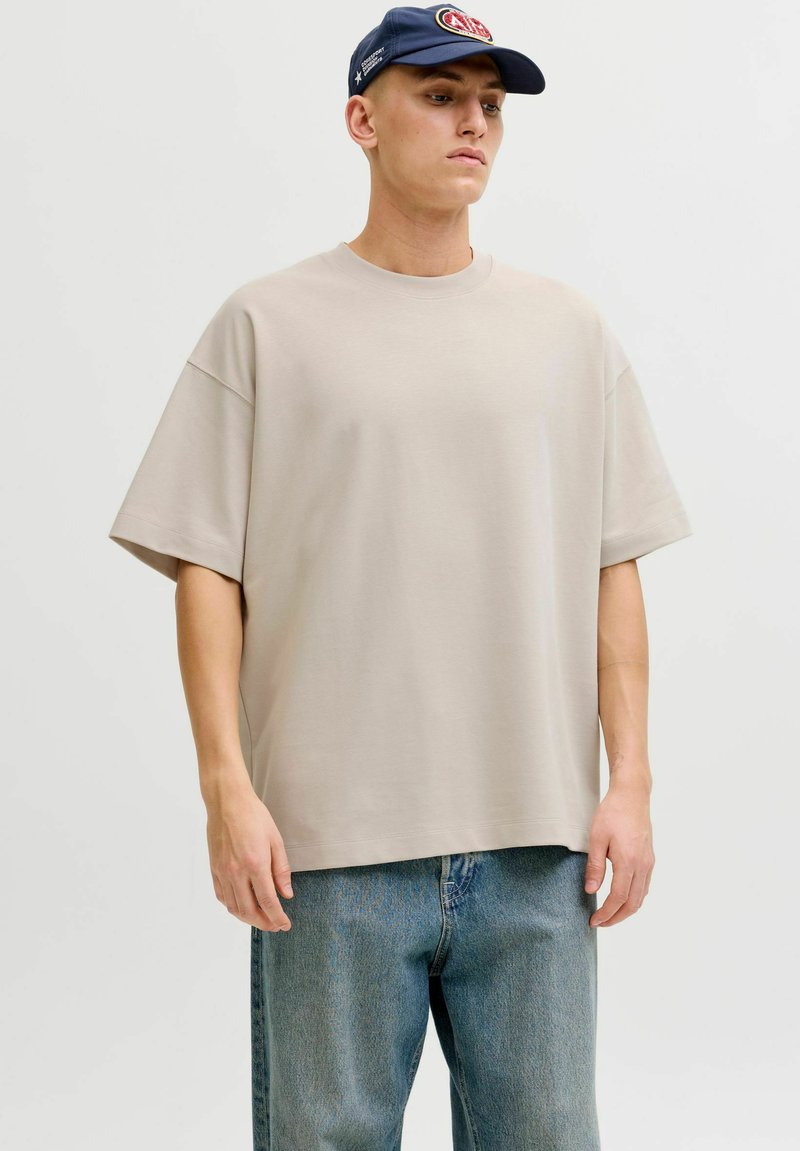 T-shirt beige oversize en coton, avec des manches courtes et un col ras du cou, associé à un jean en denim bleu clair.