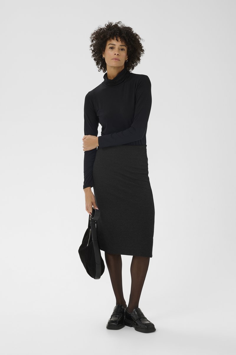 Must turtleneck top koos põlveni ulatuva tekstuurse tumeda seelikuga. Modell kannab musti kingi ja hoiab musta kotti. Minimalistlik disain.