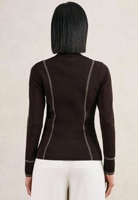 Brązowy sweter z długim rękawem, z białymi przeszyciami kontrastowymi wzdłuż szwów i dopasowanym krojem, w zestawie z off-white spodniami.