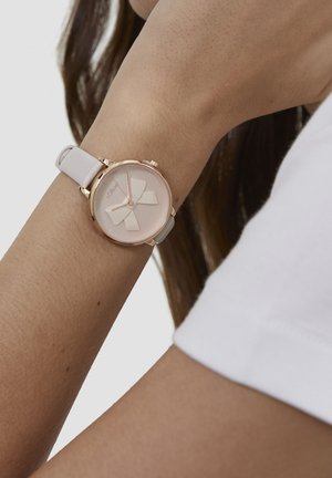 Ronde horloge met een kast van roségoud, een lichtroze wijzerplaat met een strikontwerp en een lichtgrijze leren band.