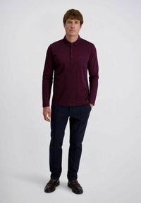 Bordeaux langemouw polo-shirt met een kraag en een borstzak, gecombineerd met marineblauwe broek en een paar bruine loafers. Gladde stofstructuur.