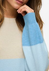 Lekki sweter z dzianiny z prążkowanym dekoltem i rękawami. W kolorach beżowym i odcieniach niebieskiego, z miękkim, teksturowanym wykończeniem.