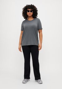 Gray short-sleeve t-shirt with a relaxed fit, paired with black pants and silver sneakers. Background is plain white.