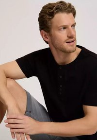 Czarny t-shirt henley z krótkim rękawem i pięcioma guzikami, w zestawie z szarymi szortami. Gładka tekstura, swobodny design, dopasowany fason.