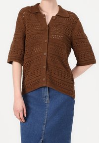 Cárdigan marrón de punto con mangas cortas, diseño de tejido abierto y cierre de cinco botones. Cuenta con un cuello clásico y detalles texturizados.