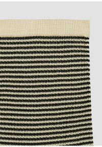 Tissu tricoté avec des rayures horizontales noires et crème et une bordure côtelée crème unie en haut, présenté sur un fond gris clair.