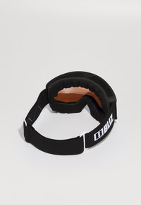 Lunettes de ski noires avec un cadre en mousse souple, verres teintés orange, et une sangle noire ajustable avec un logo blanc. Accents latéraux texturés.