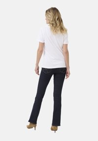 Vit bomulls t-shirt, mörkblå utsvängda jeans och beige högklackade skor. Bakifrån syns jeansen med två bakfickor och sömdetaljer.