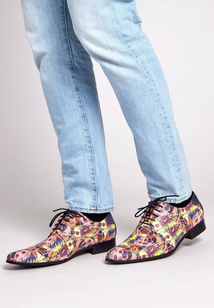 Kleurige gepatternde dress schoenen met een glanzende afwerking, zwarte veters en een vierkante neus, gedragen met lichtblauwe spijkerbroek.