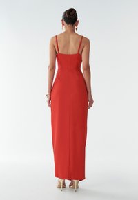 Punane satiinist maksimek, millel on sobiv rinnaosa, õhukesed rihmad ja lukuga sulgemine seljal. Seelik voolab sirgelt maani.