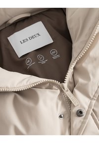 Beidzjā jaka ar iekšpusi, kurā ir uzlīme ar tekstu "LES DEUX". Iekļauj rāvējslēdzēju, pogu ar spiedpogu un ikonām, kas norāda uz izturību pret vēju, ūdensizturību un elpojamību.