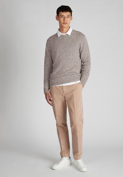 Pull en tricot gris clair, col rond, en tissu texturé ; associé à un pantalon chino beige et des baskets blanches, se tenant devant un fond uni.