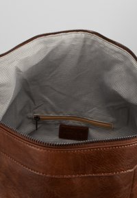 Braune Ledertasche mit gestreiftem Stofffutter, ausgestattet mit einer Reißverschlusstasche und einem Etikett. Reißverschluss oben.