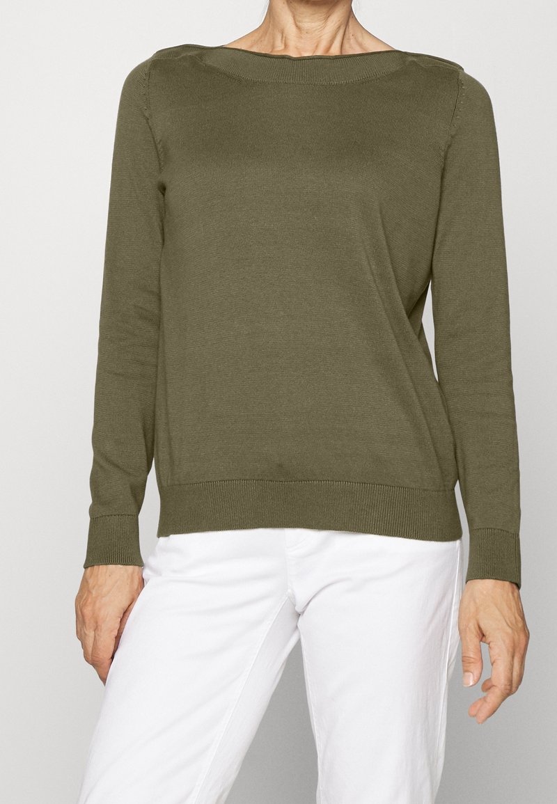 Maglione verde oliva, con scollatura e polsini a coste, dalla texture morbida, maniche lunghe, vestibilità rilassata, abbinato a pantaloni bianchi.
