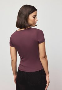 Tumepruun lühikeste varrukatega särk, millel on keha järgiv lõige ja ümar kaelus, valmistatud siledast kangast. Kandmiseks kokku mustade kõrge vöökohaga pükstega.