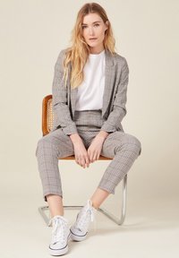 Ruudullinen puku beigen ja ruskean sävyissä, jossa on hyvin istuva takki ja kapeat housut, yhdistetty valkoiseen t-paitaan ja valkoisiin lenkkikengiin.