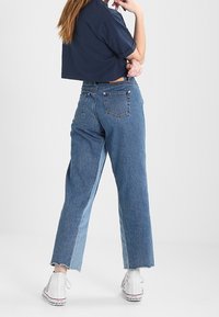 Klippt marinblå skjorta i kombination med hög midja blå jeans med en blekt tvätt, fransad fåll och vita hög-top sneakers.