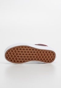 Semelle extérieure en caoutchouc brun avec un motif en losange, entourée d'une semelle intermédiaire blanche et d'une tige en tissu rouge, avec une bande latérale et des détails en mesh.