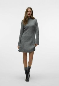 Robe tricotée grise avec texture côtelée, col montant et manches longues. Présente des fentes latérales et tombe au-dessus du genou, associée à des bottes noires.
