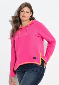Rosa Kapuzenpullover mit kontrastierendem orangefarbenem Innenfutter, ausgestattet mit einer Kordelzugkapuze, seitlichen Reißverschlüssen und einem schwarzen Logopatch am Saum.