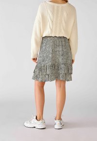 Cremefarvet kabelstrikket sweater med oversize design, kombineret med en sort-hvid mønstret flæse-nederdel og hvide atletiske sneakers.