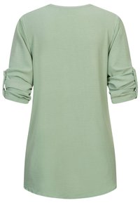 Camicia verde chiaro a maniche lunghe con polsini arrotolati. Tessuto morbido e testurizzato; scollatura arrotondata; orlo leggermente curvo nella parte inferiore.